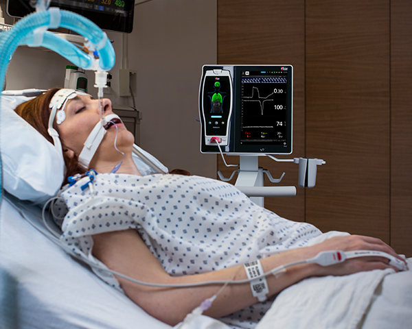 Paziente intubato addormentato in un letto d'ospedale, monitorato tramite un sensore da dito con monitoraggio al posto letto Root e Radical-7.