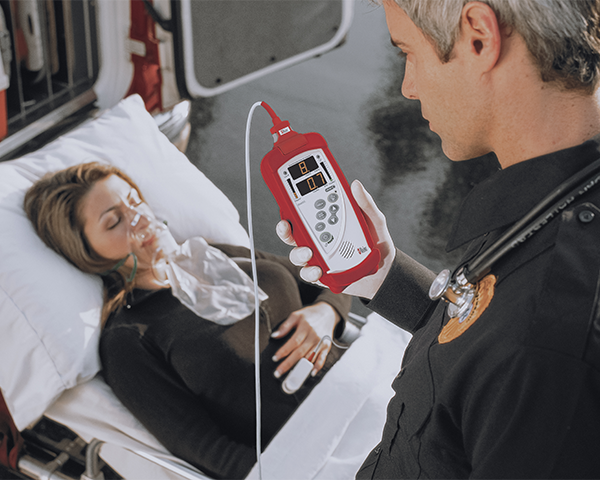 Operatore d'emergenza che esegue il monitoraggio di un paziente privo di coscienza su una barella accanto a un'ambulanza.