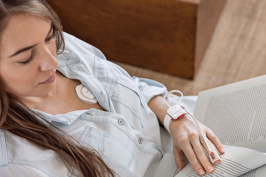 Masimo - Woman in chair with Masimo SafetyNet on her wrist while reading a book