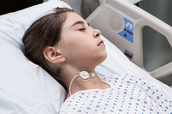 Masimo - Paziente pediatrico con il sensore per il monitoraggio acustico della frequenza respiratoria RRa applicato al collo in un letto ospedaliero